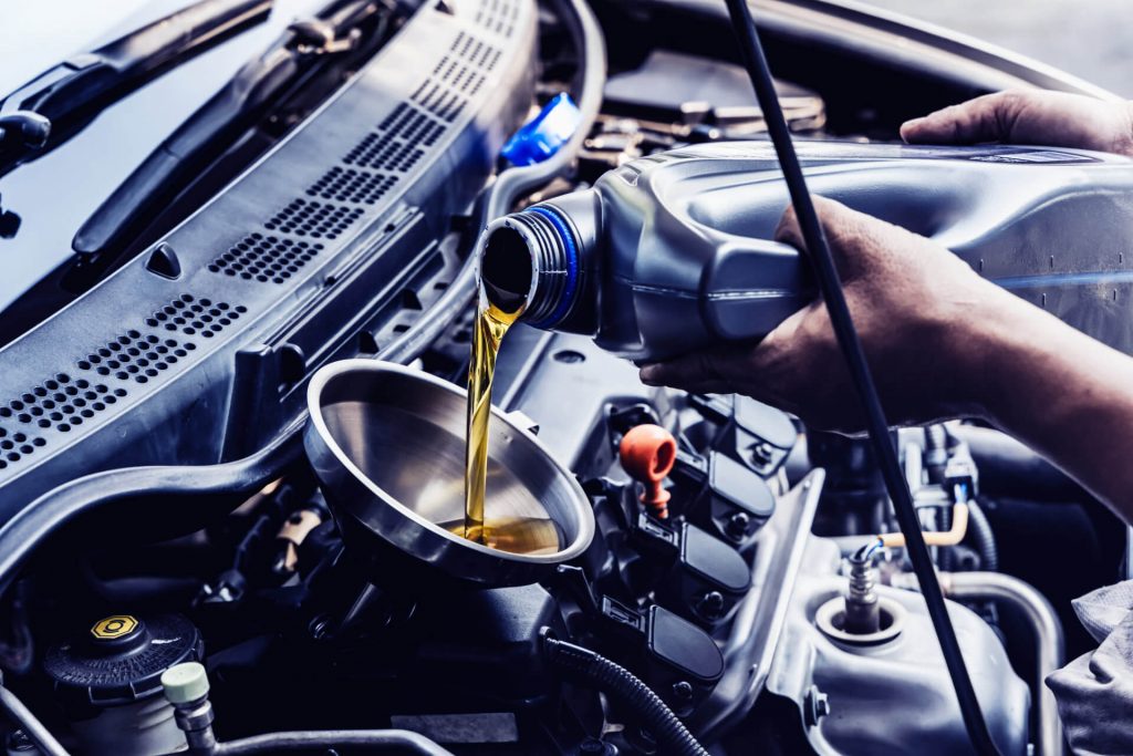 Car mechanic pouring engine oil into vehicle during doing car maintenance in garage